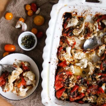 A cauliflower casserole dish with tomatoes, vegetables, and a spoon.