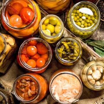 Different preserved vegetables from vegetables and mushrooms in glass jars on a wooden background.