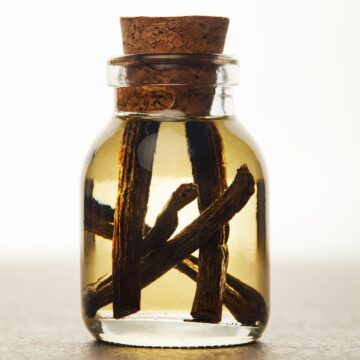 A glass bottle with homemade vanilla extract and cinnamon sticks in it.