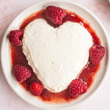 A heart shaped dessert with raspberries and cream on a plate.